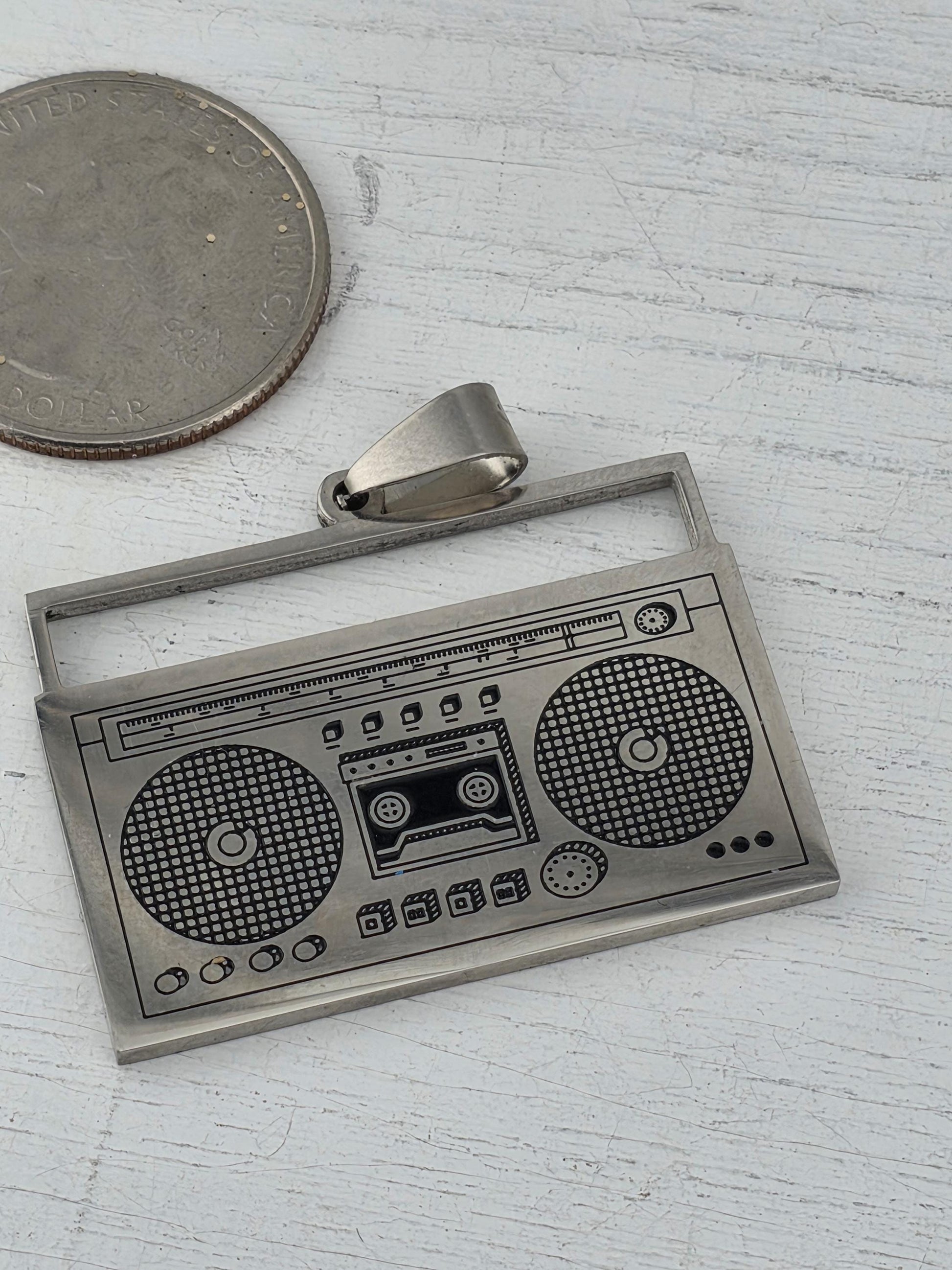 a pendant in the shape of a stereo or DJ controller, with a coin placed next to it on a white surface.