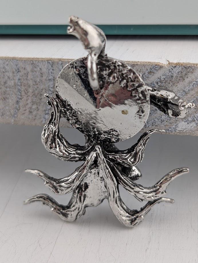 A silver metal sculpture of an octopus with its tentacles spread out, sitting on a white surface.