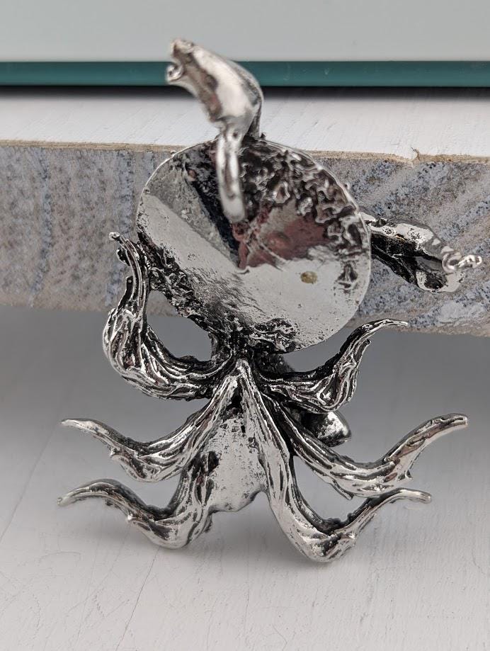 A silver metal sculpture of an octopus with its tentacles spread out, sitting on a white surface.