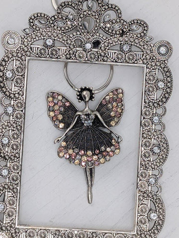 A silver-colored pendant featuring a stylized fairy figure with wings and a flowing dress, adorned with numerous small, colorful gemstones.