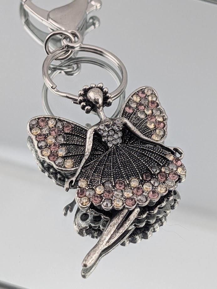 A silver-colored pendant featuring a stylized fairy figure with wings and a flowing dress, adorned with numerous small, colorful gemstones.