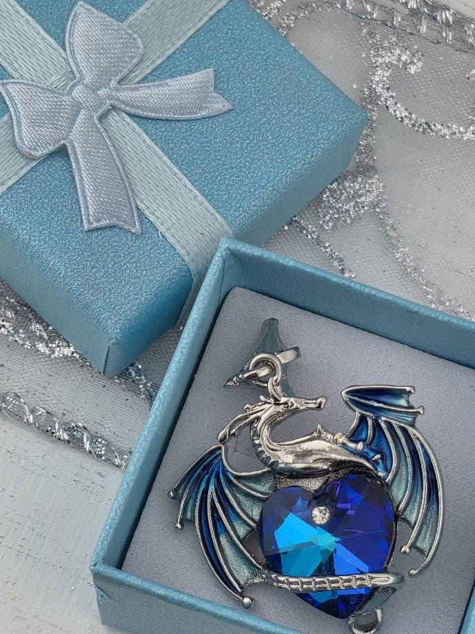 a blue gift box with a silver dragon pendant inside, placed on a white surface.