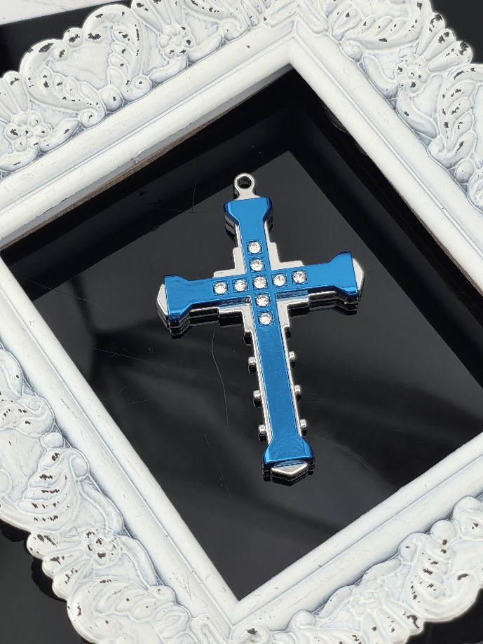 A blue and silver cross pendant with rhinestones is displayed in a white ornate frame against a black background.