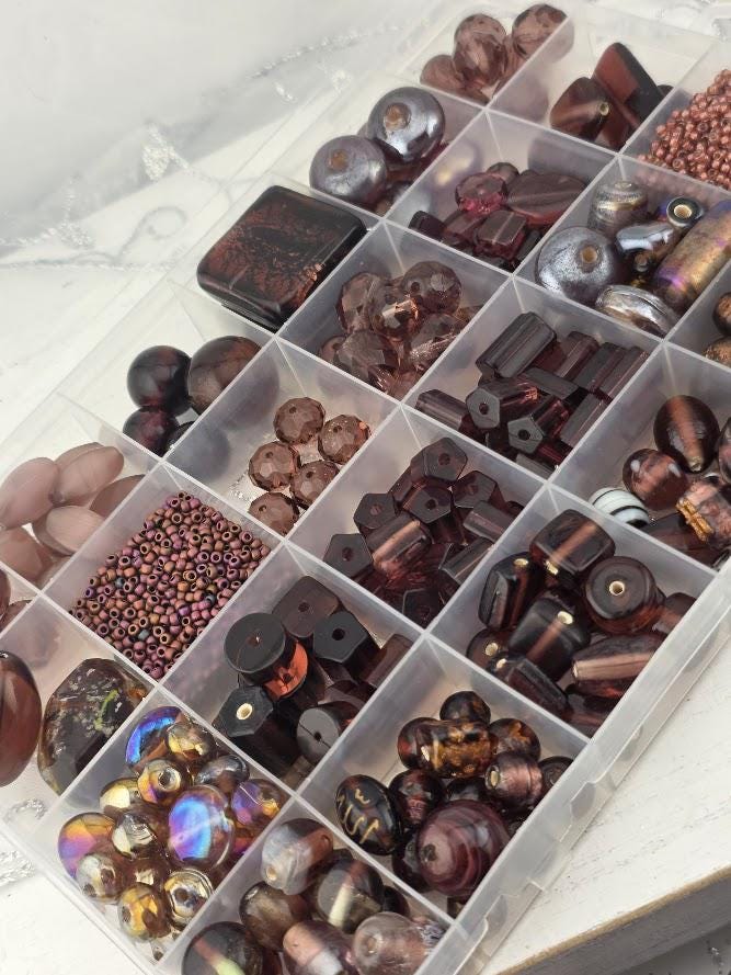 A clear plastic container filled with various beads and beads in different shapes and sizes, organized in rows and columns.