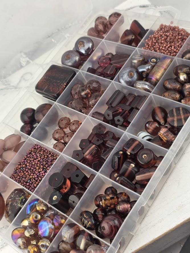 A clear plastic container filled with various beads and beads in different shapes and sizes, organized in rows and columns.