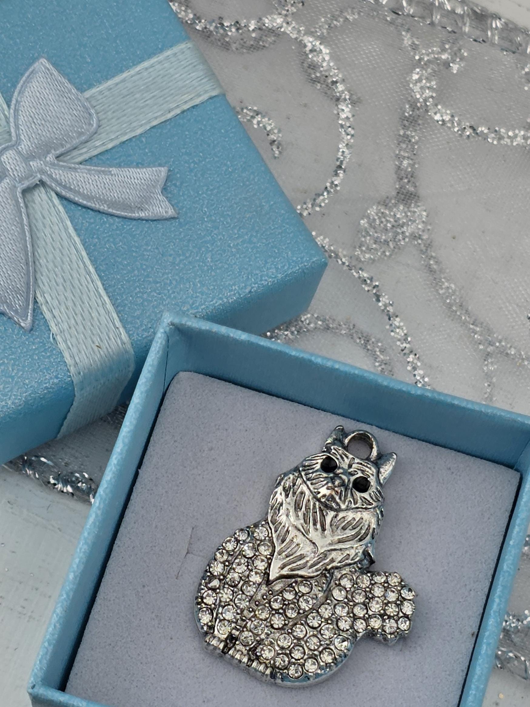 A silver pendant in the shape of a cat is displayed in a blue gift box with a white ribbon bow.