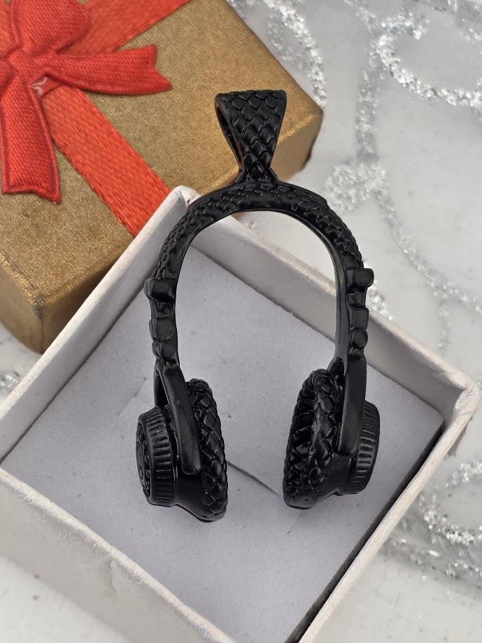A pair of black headphones is displayed in a white box, with a gold gift box and a red ribbon visible in the background.