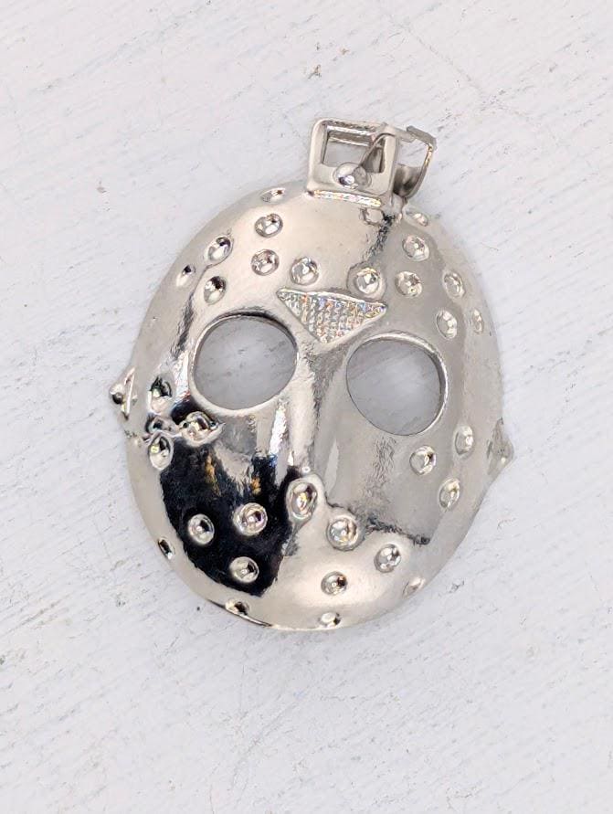 A silver pendant in the shape of a mask with a diamond-like design on the front.