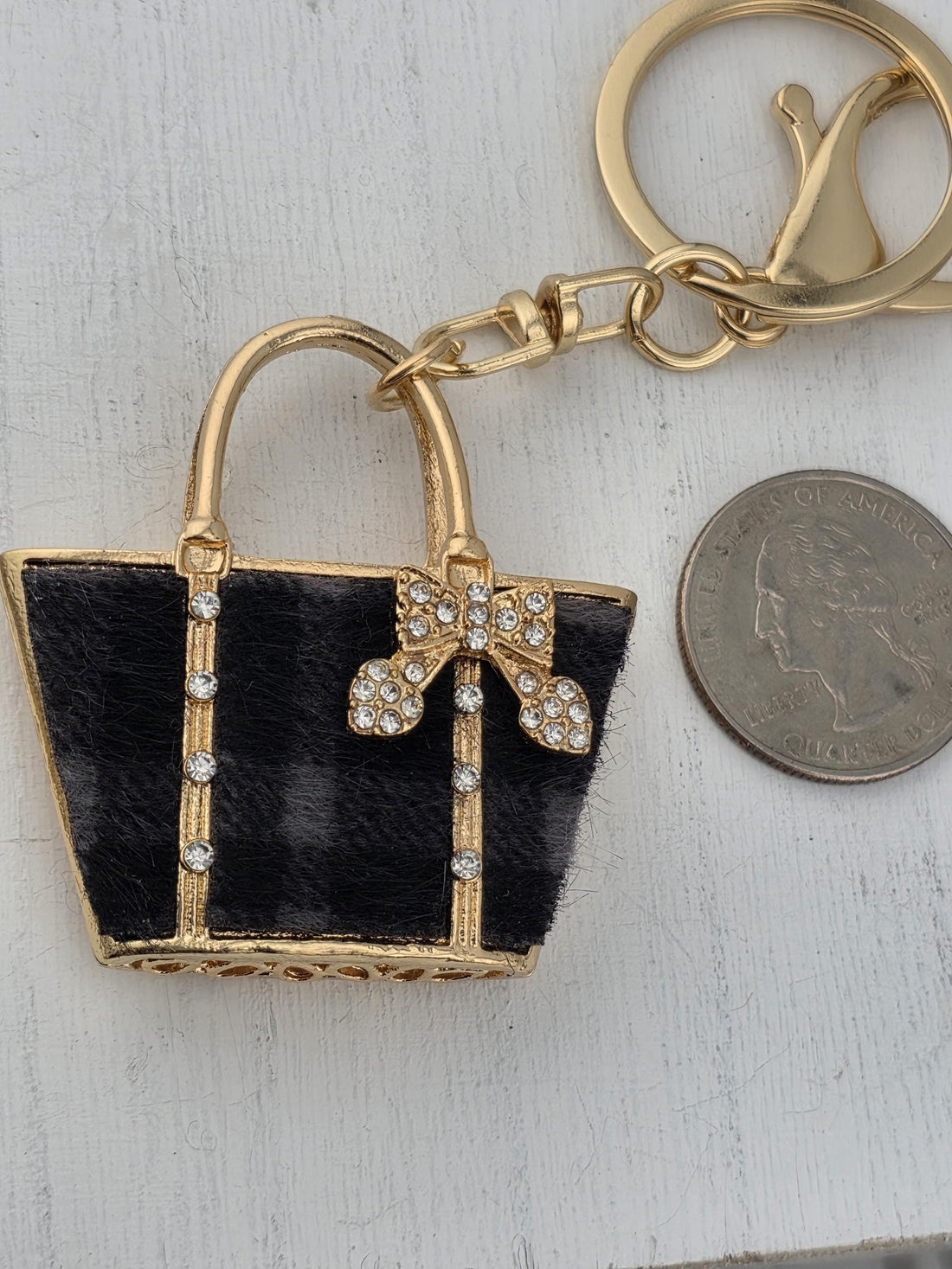 A gold-colored keychain with a black fur-like material and a gold bow on it, attached to a white surface.