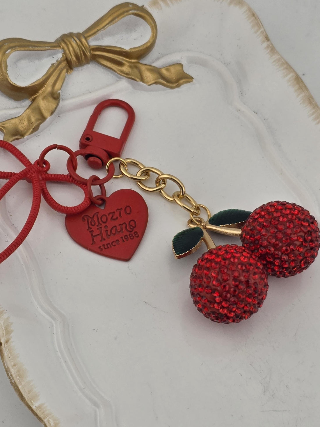 A decorative keychain with a red heart-shaped charm and two red crystal balls, placed on a black surface with a silver frame.