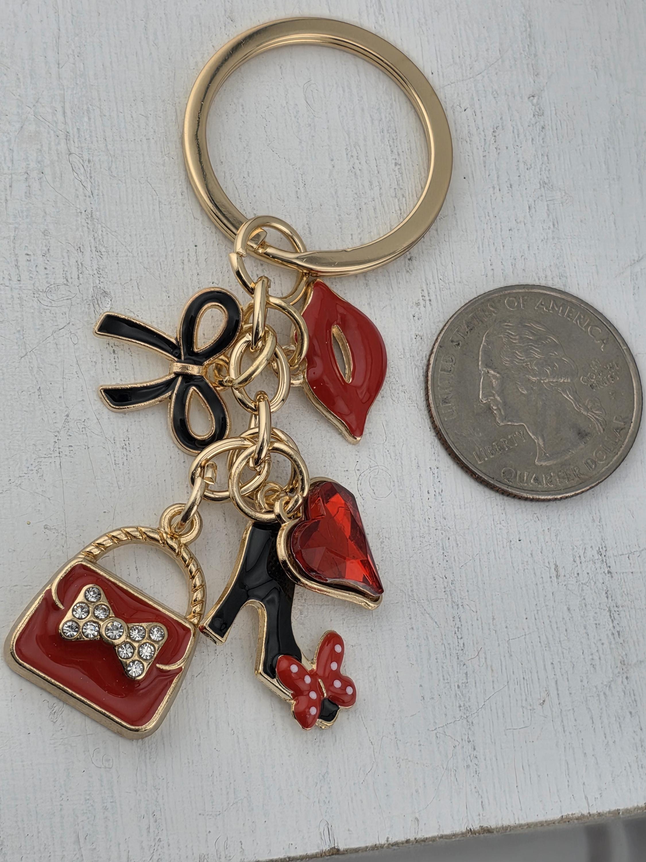 A keychain with various decorative charms, including a red bow, a red heart, and a red butterfly, along with a coin and a small bag.
