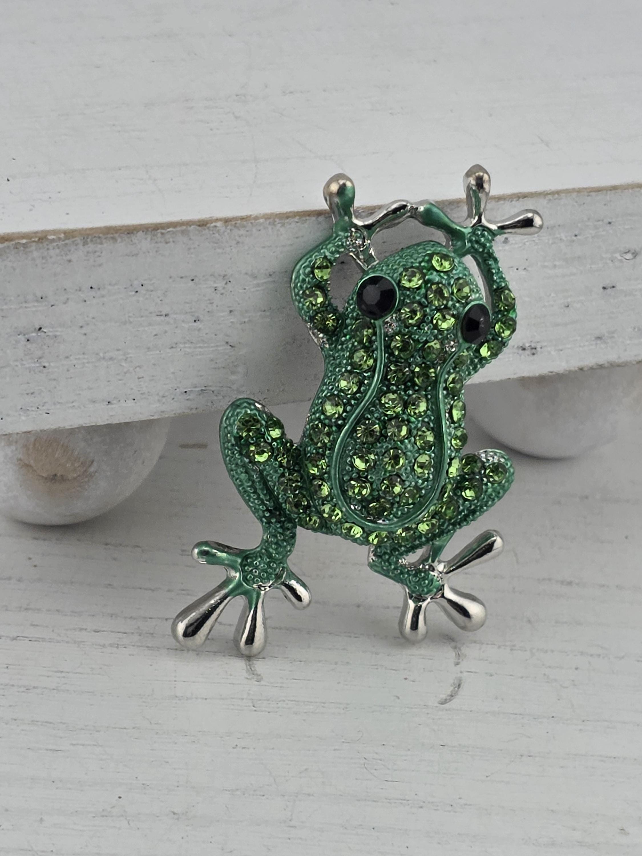 A green frog brooch with rhinestones is displayed on a white surface.