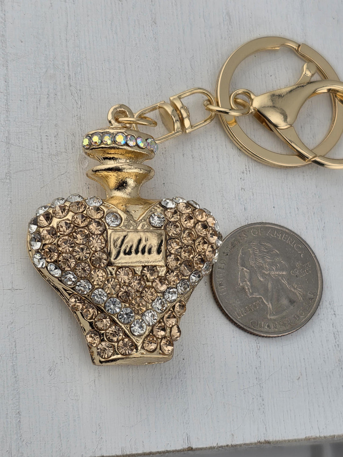 A decorative gold-colored perfume bottle keychain with rhinestones and a small coin placed next to it on a white surface.