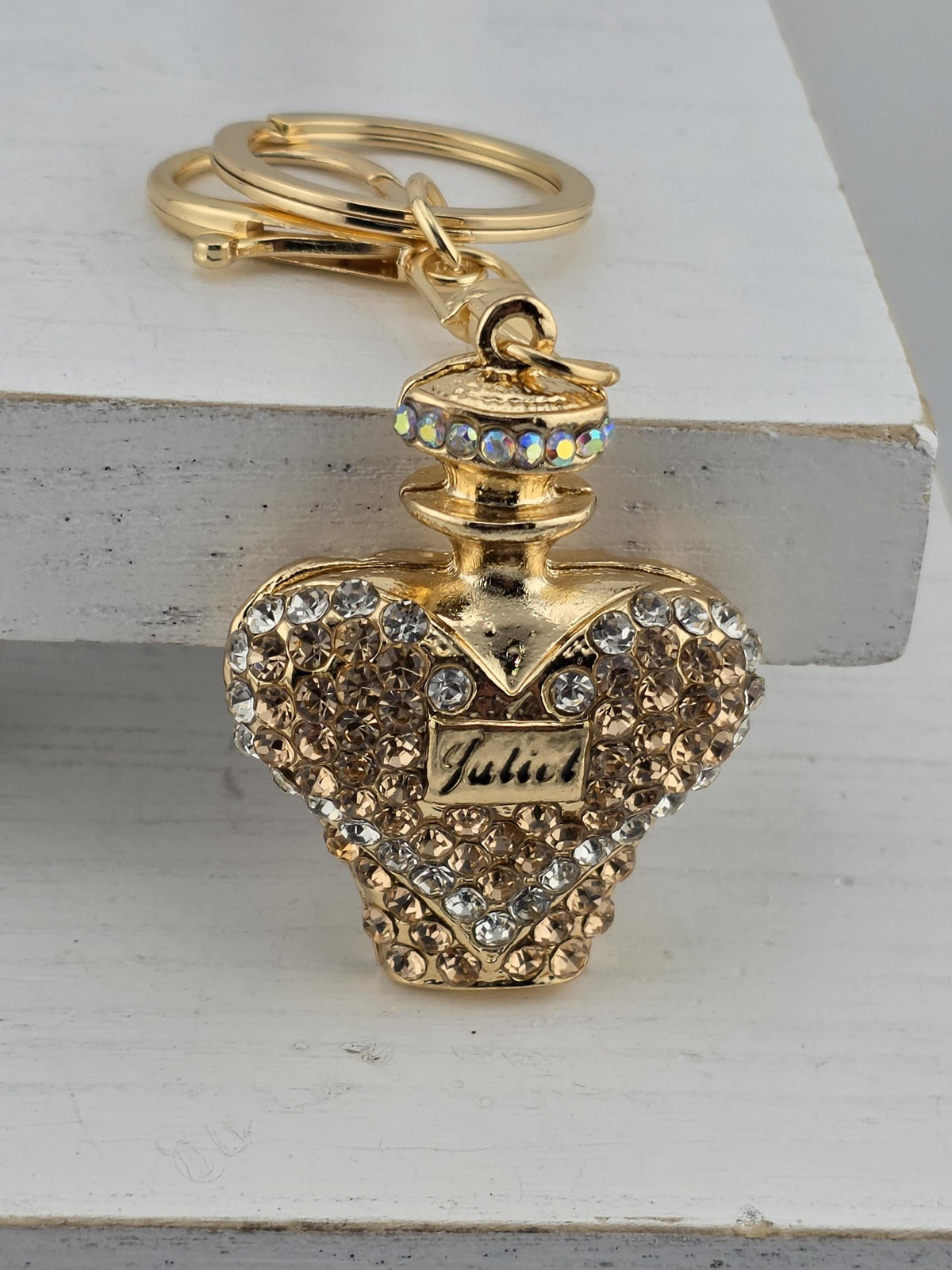 A decorative keychain with a gold-colored pendant adorned with rhinestones and a small label.