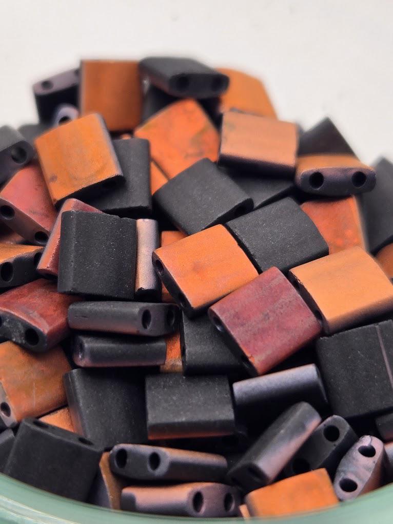 A close-up image of a pile of colorful beads, including orange, black, and brown pieces, arranged in a visually appealing manner.