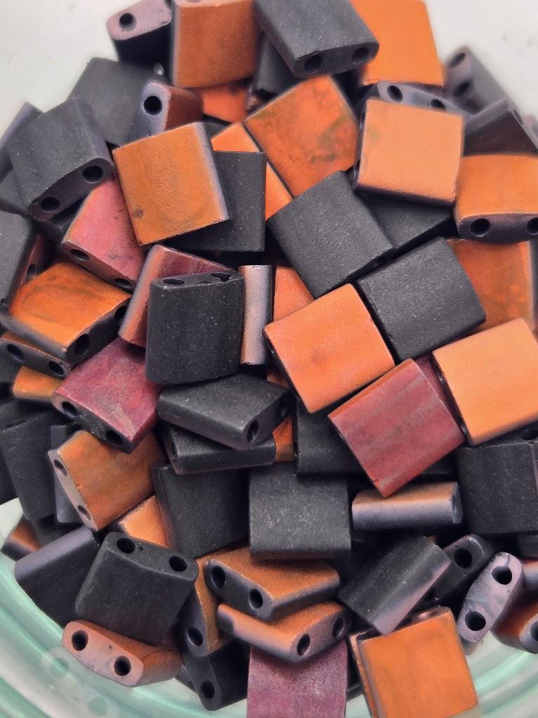 a close-up view of a pile of small, colorful beads in various shades of orange, black, and purple.