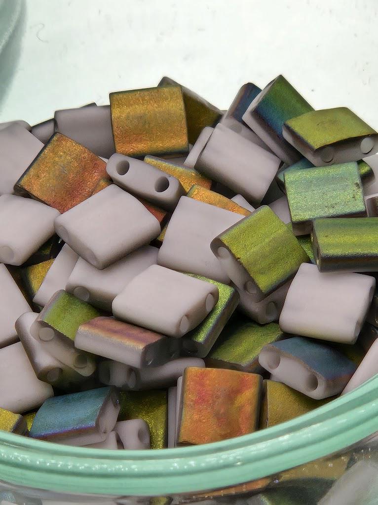 A pile of colorful glass beads in various shades of green, purple, and orange.