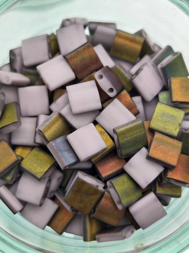 A glass jar filled with small, colorful beads in various shades of gray, green, and orange.