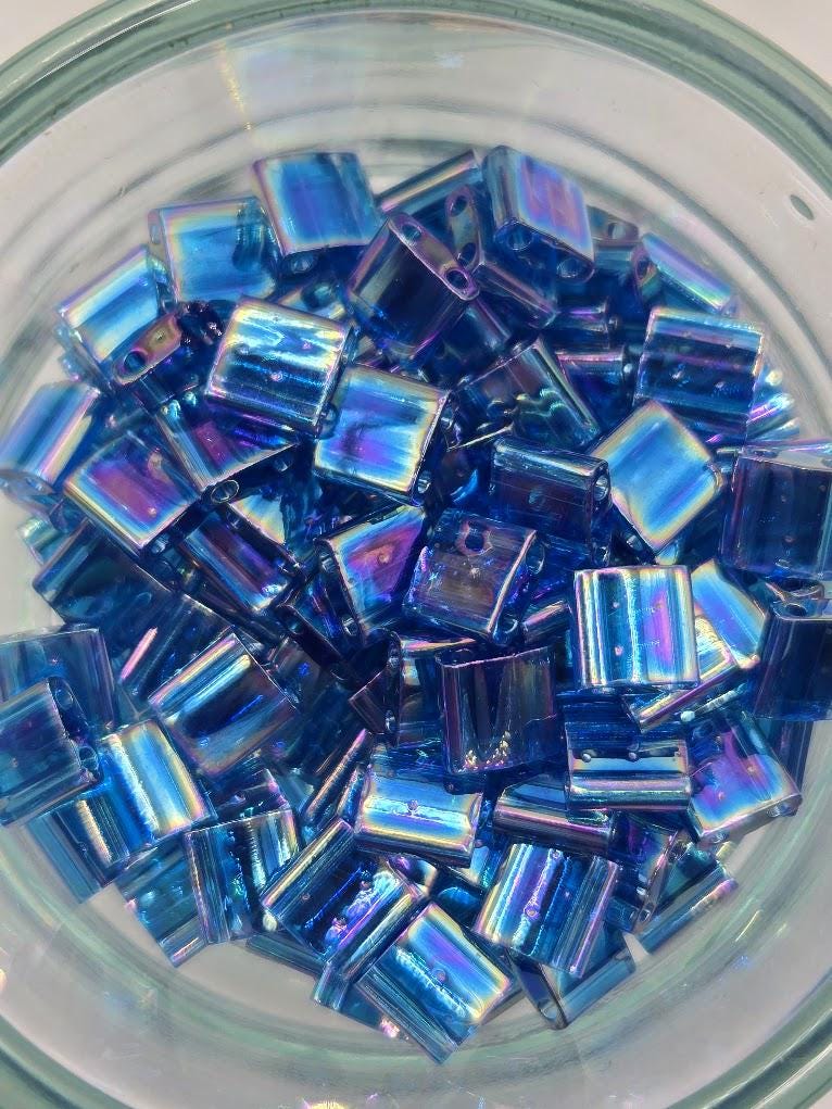 A glass bowl filled with numerous small, square-shaped blue beads.