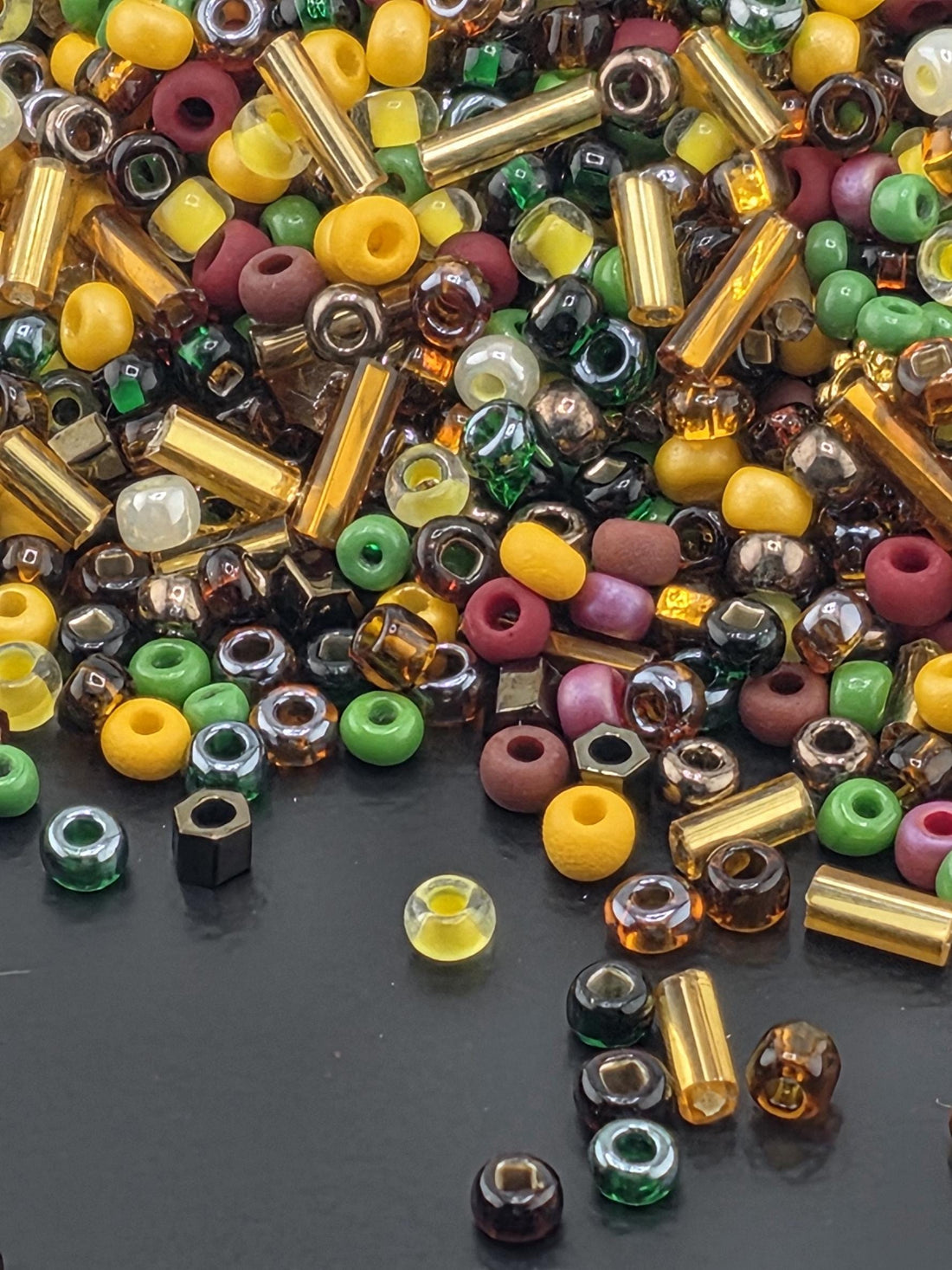 A colorful assortment of beads, including glass, metal, and plastic, scattered on a dark surface.