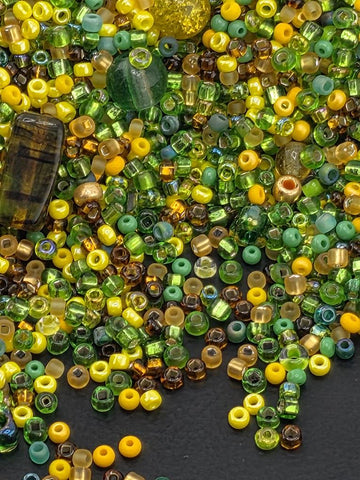 The image is a collection of various colored beads, including green, yellow, and brown, scattered on a dark surface.