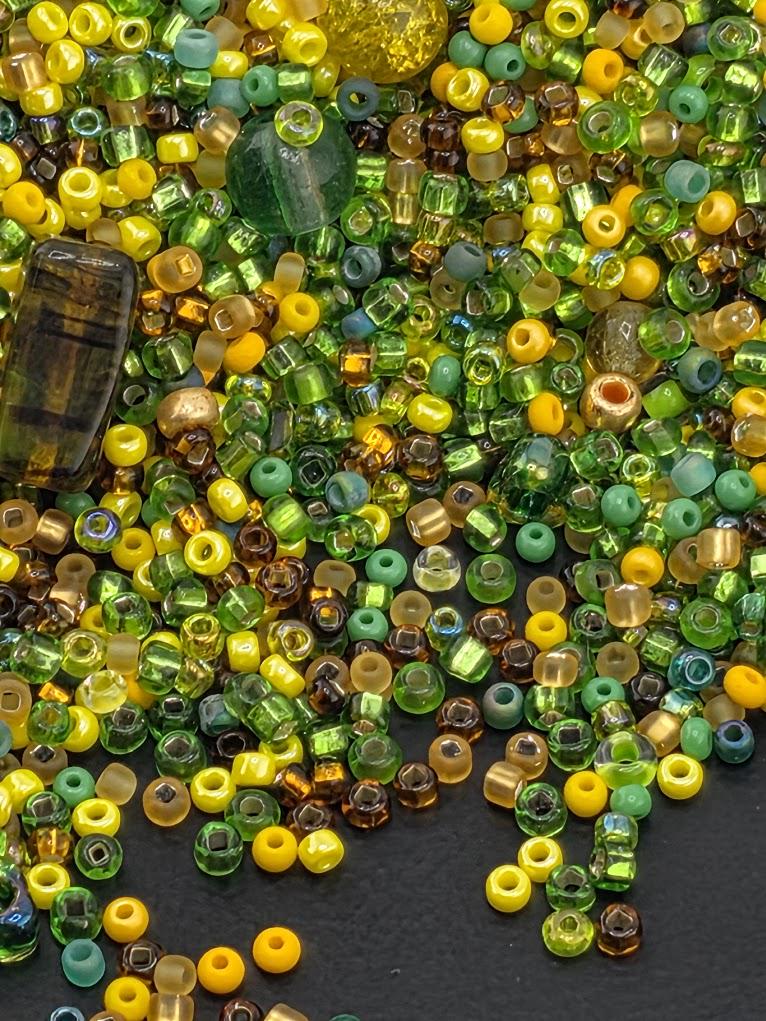 The image is a collection of various colored beads, including green, yellow, and brown, scattered on a dark surface.