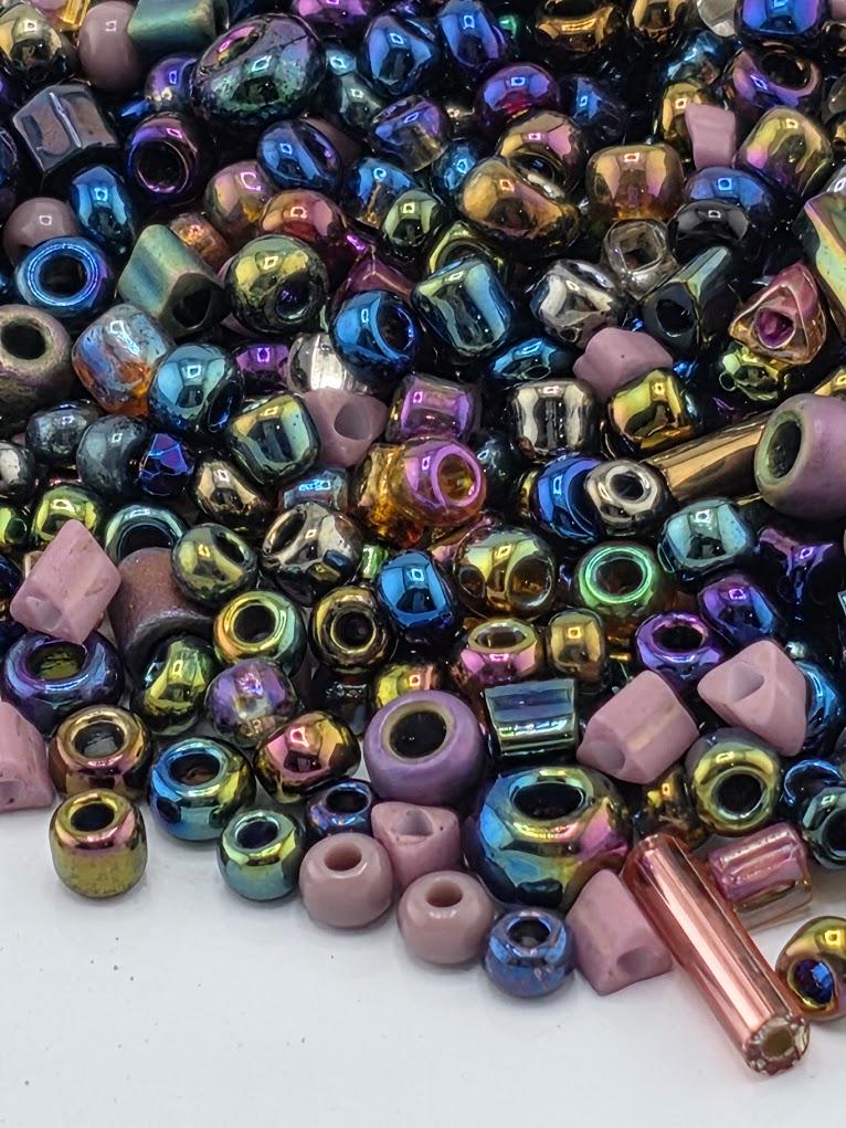A colorful assortment of multicolored beads, including metallic and glass beads, scattered on a surface.