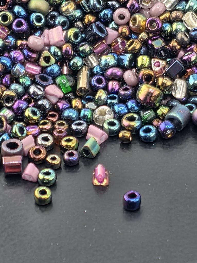 A colorful assortment of multicolored beads, including glass beads and metal beads, scattered on a dark surface.