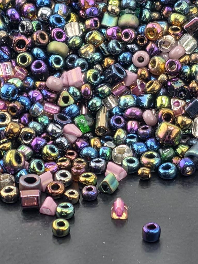 A colorful assortment of multicolored beads, including glass beads and metal beads, scattered on a dark surface.