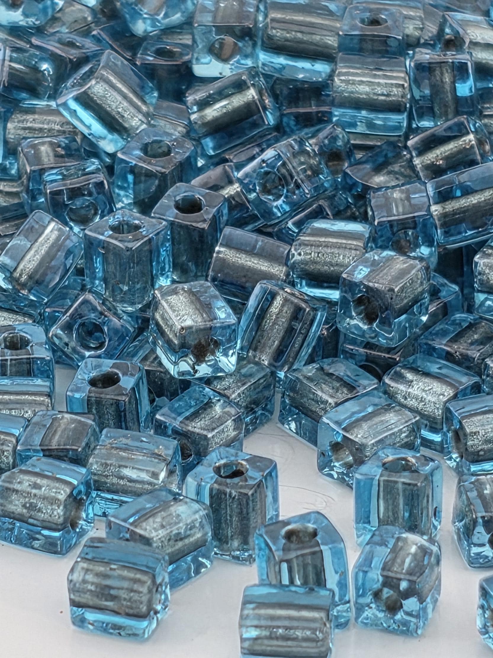 The image is a close-up of numerous blue and silver glass beads, with their interlocking shapes creating a visually striking pattern.