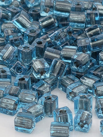 The image is a close-up of numerous blue and silver glass beads, with their interlocking shapes creating a visually striking pattern.