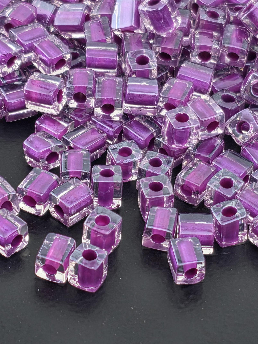 a close-up view of numerous clear glass beads in shades of purple, scattered on a dark background.