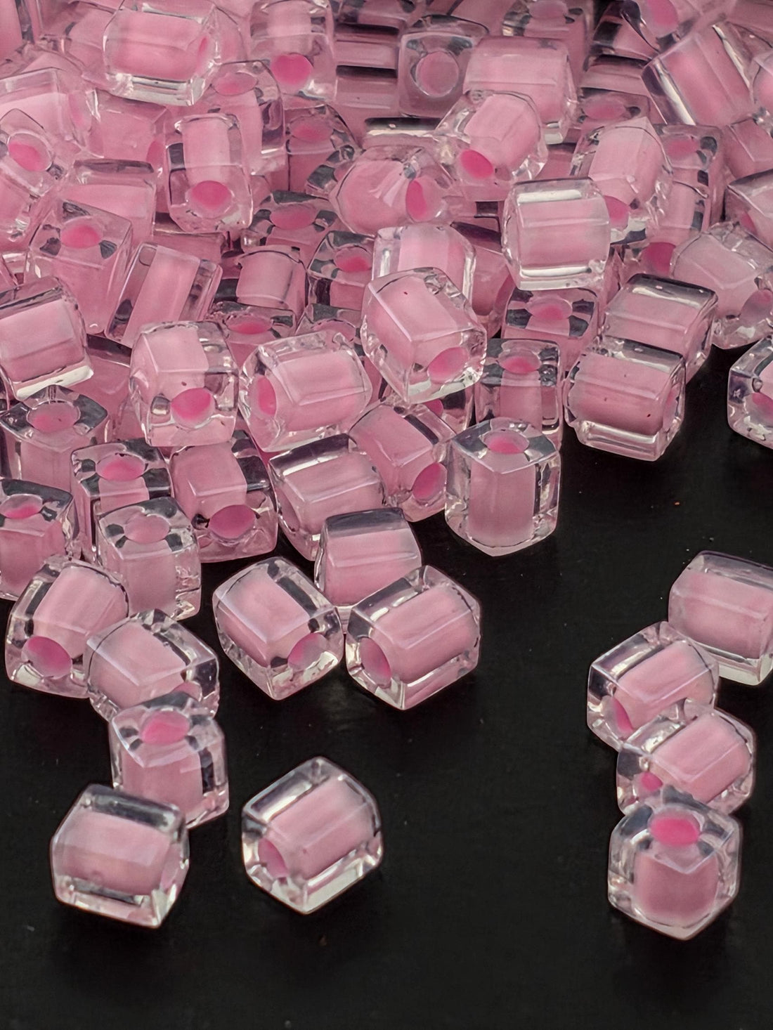 a close-up view of numerous clear, transparent, and pink-colored cubes or beads scattered on a dark background.
