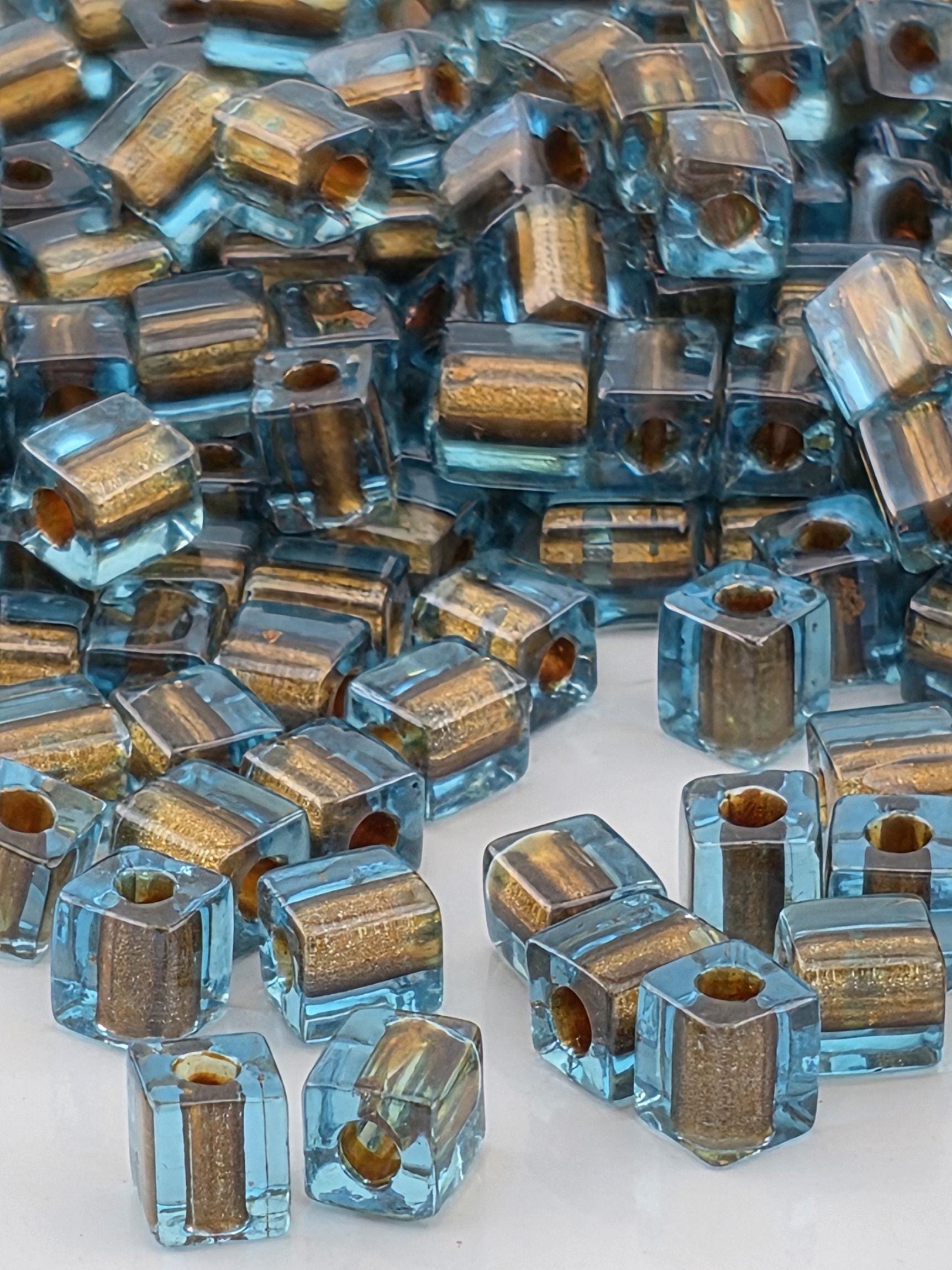 The image is a close-up of numerous small, clear glass beads in various shades of blue and gold, scattered across a surface.