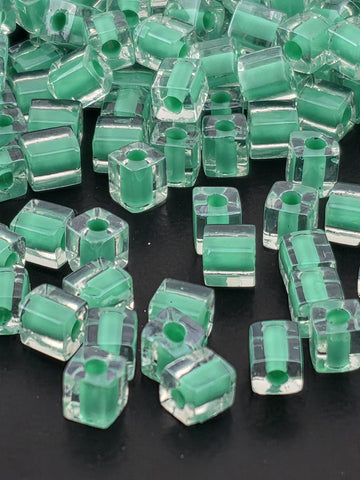 a collection of clear glass beads in various shades of green, scattered on a dark background.