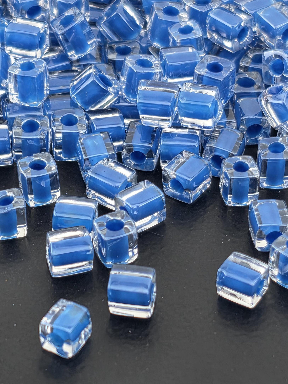 a collection of clear glass beads in various shades of blue, scattered on a dark background.