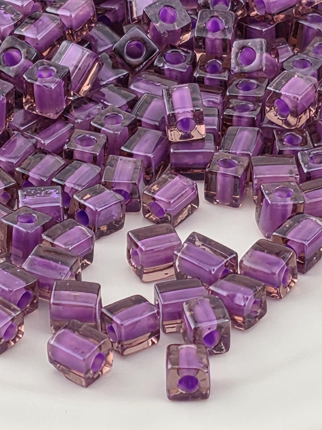 a close-up view of numerous small, clear, purple-colored glass beads or cubes scattered across a surface.