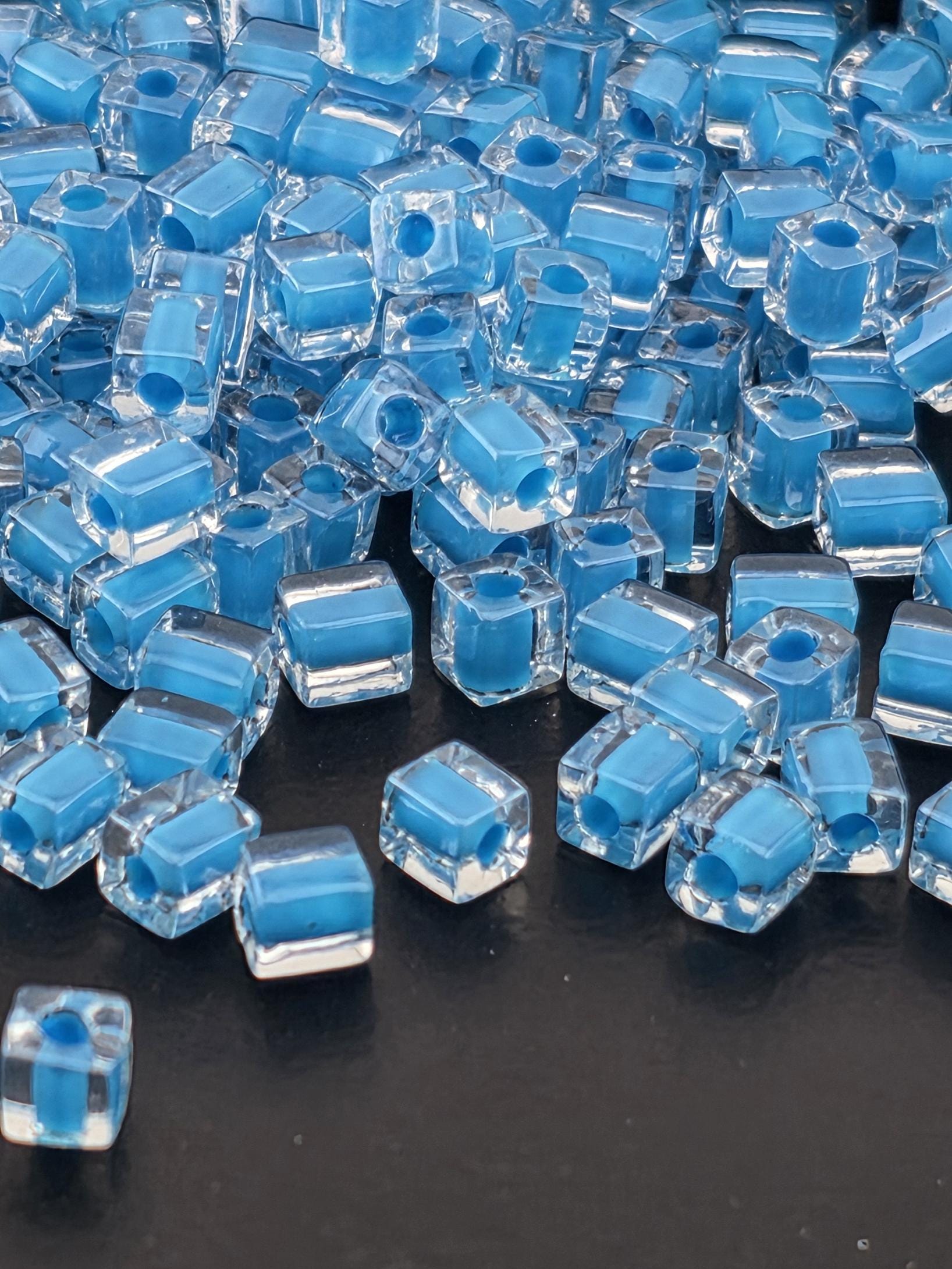 a close-up view of numerous clear, blue glass beads scattered on a dark surface.