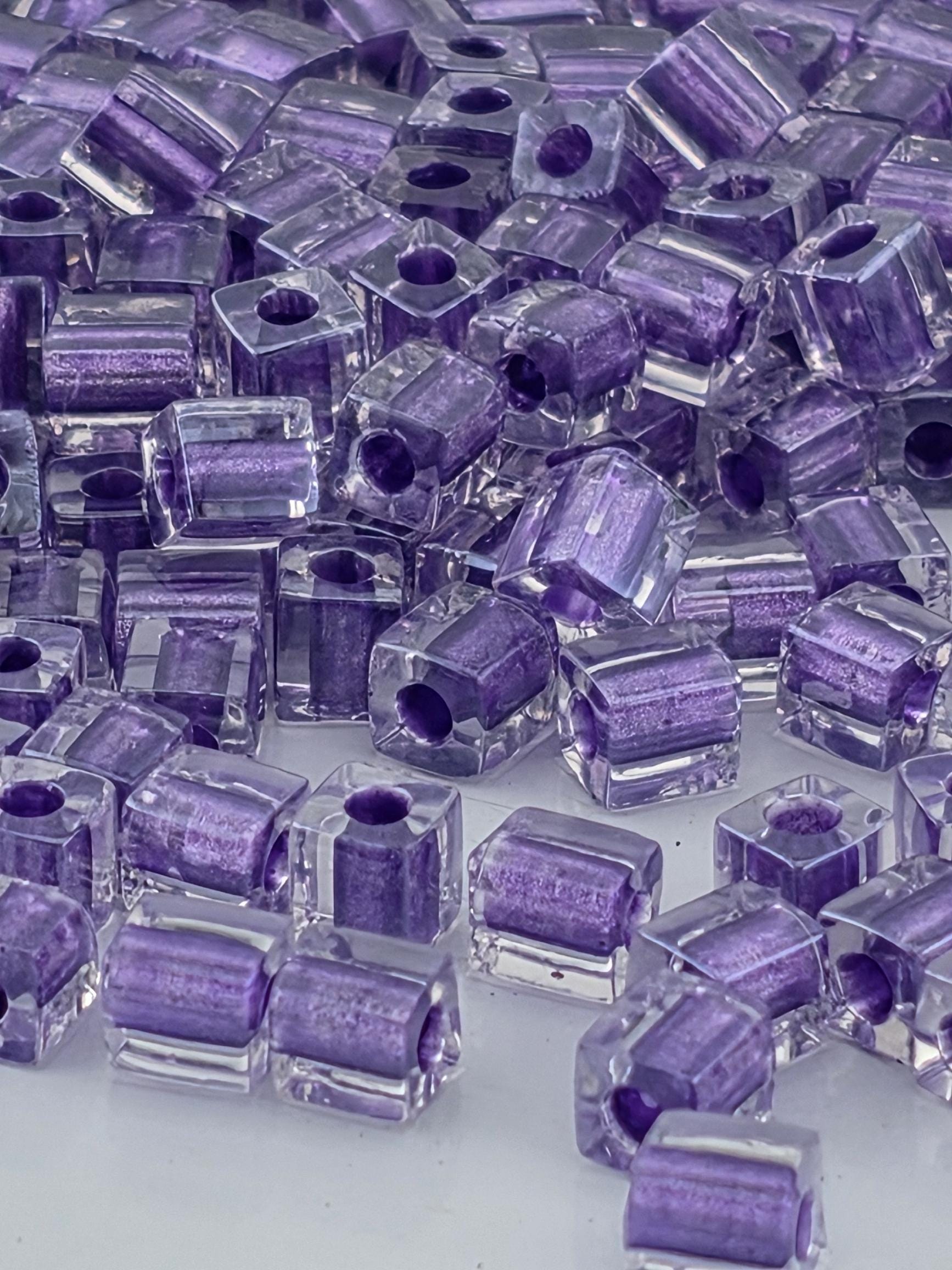 The image is a close-up of numerous clear, purple-colored glass beads or beads, scattered and overlapping each other.