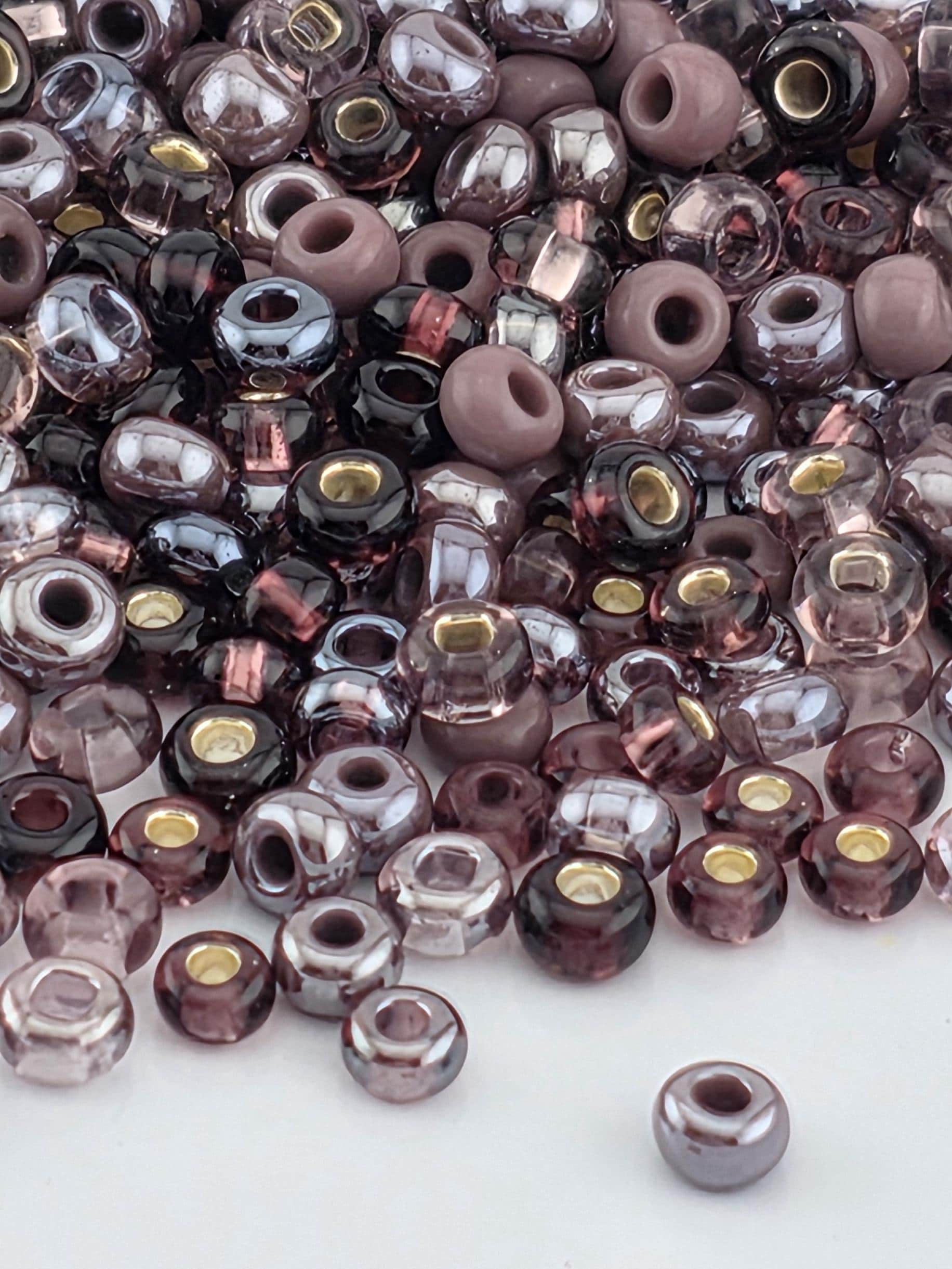 a large pile of various colored glass beads, including shades of purple, pink, and gray, scattered across a surface.