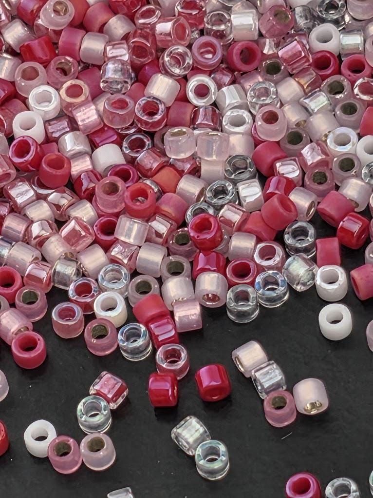 The image is a close-up of a pile of various colored beads, including clear and pink beads, scattered on a dark surface.