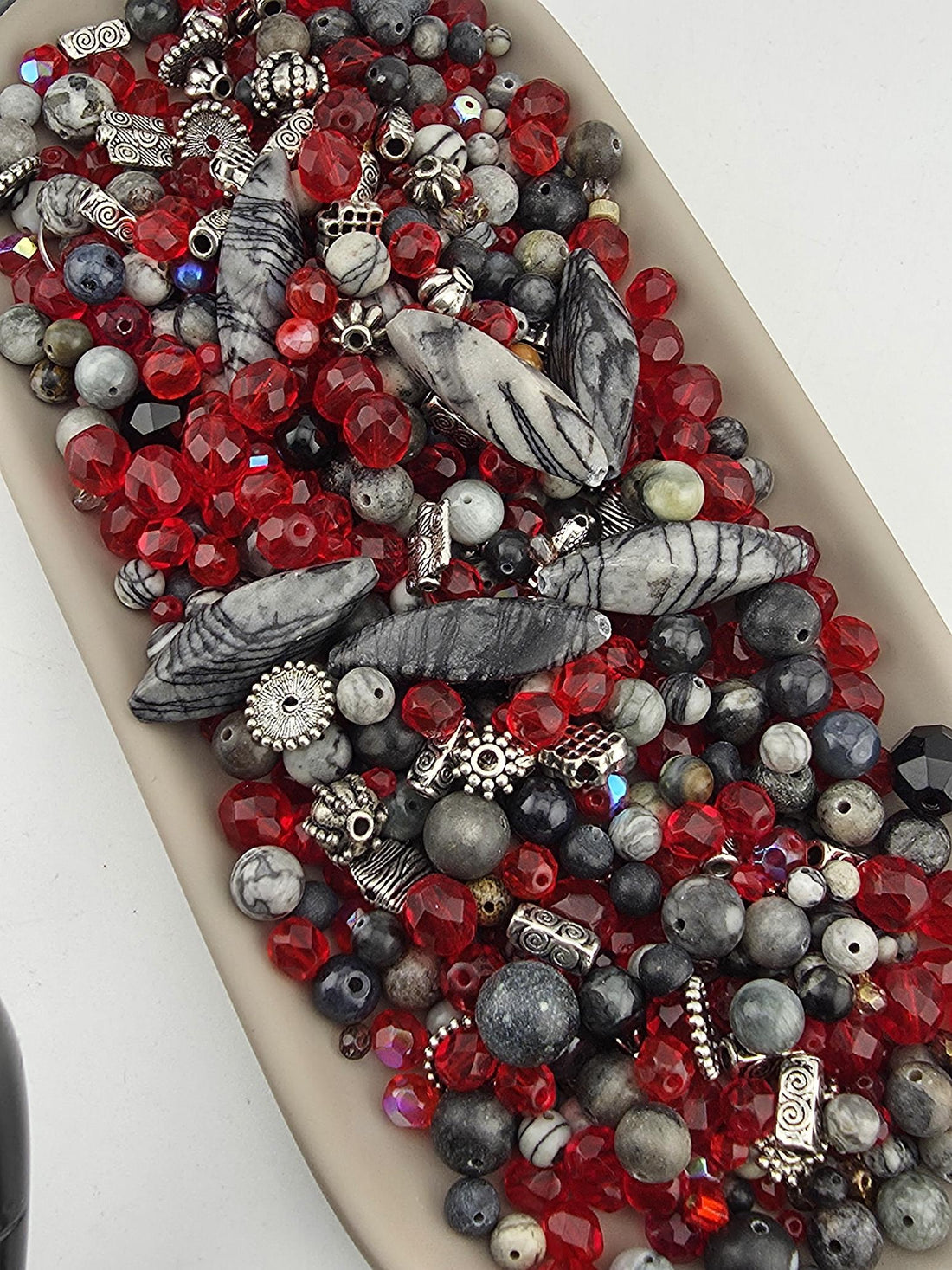 A collection of various beads, including red, black, and gray beads, as well as some silver and black beads, arranged on a surface.