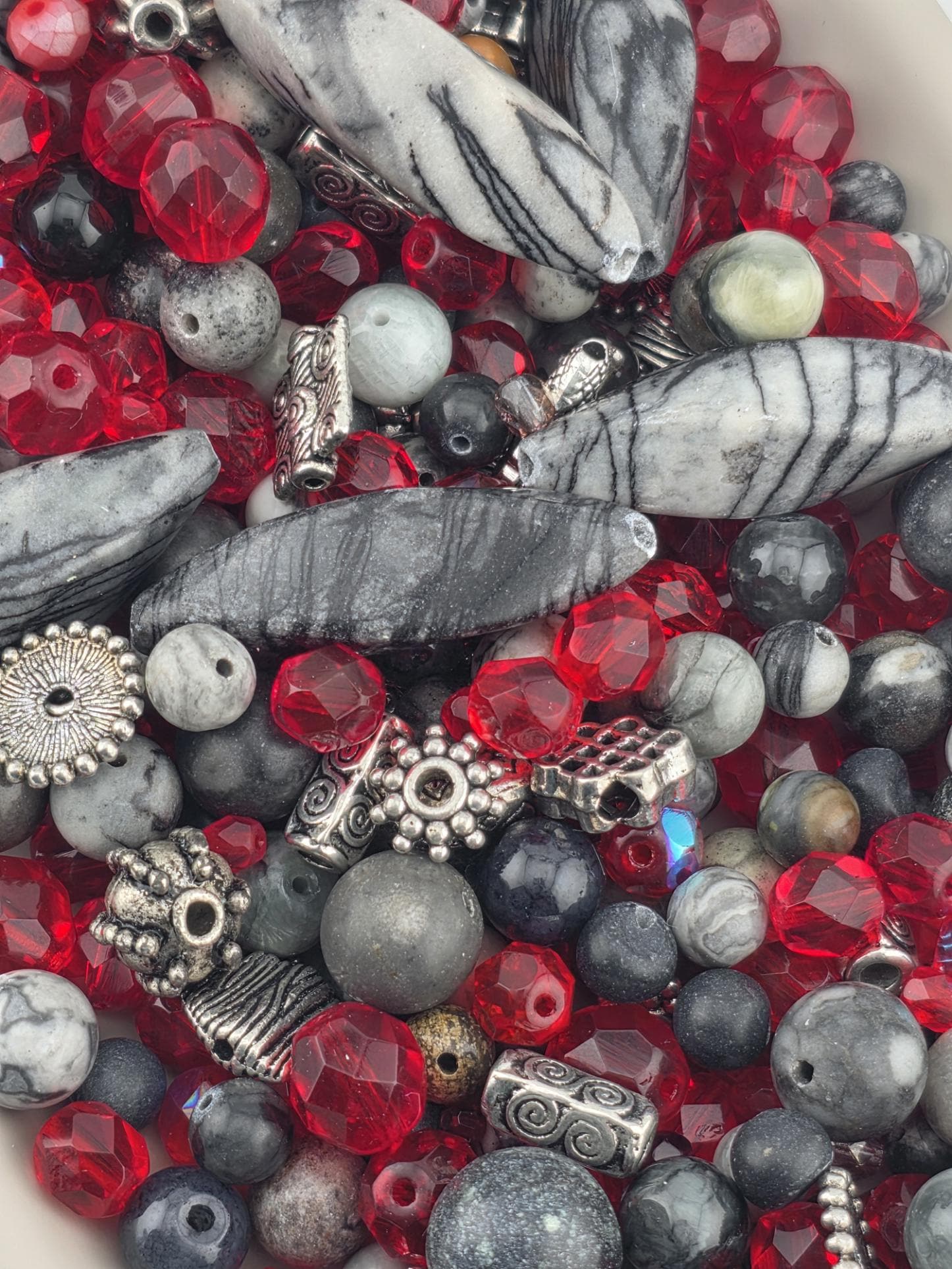 The image is a close-up of various beads and beads, including red, gray, and silver beads, as well as some with gemstones.