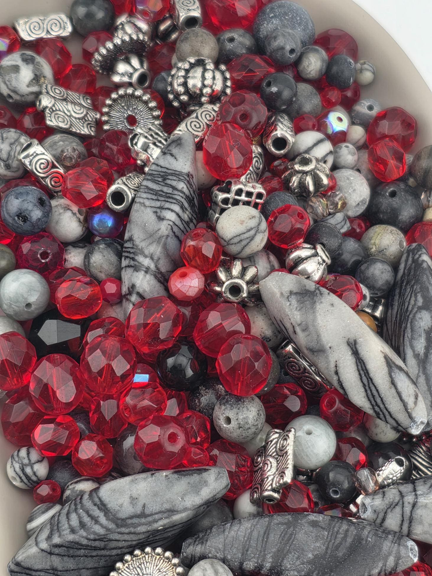 A close-up image of a variety of beads and beads in different shapes, sizes, and colors, including red, black, and gray beads.