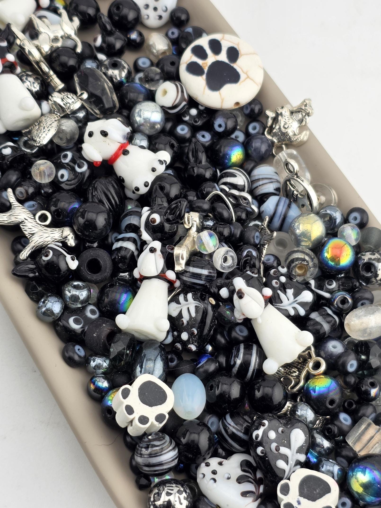 A collection of various beads, charms, and other decorative items in shades of black and white, including small animal figurines and other playful elements.