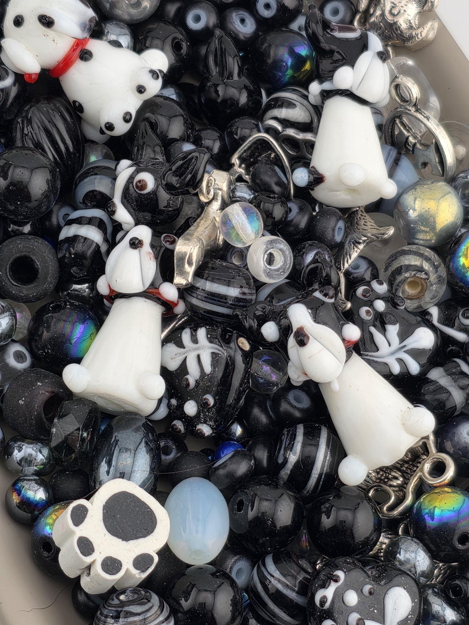 The image is a collection of various beads and charms, including black and white beads, glass beads, and metal charms, all arranged together.