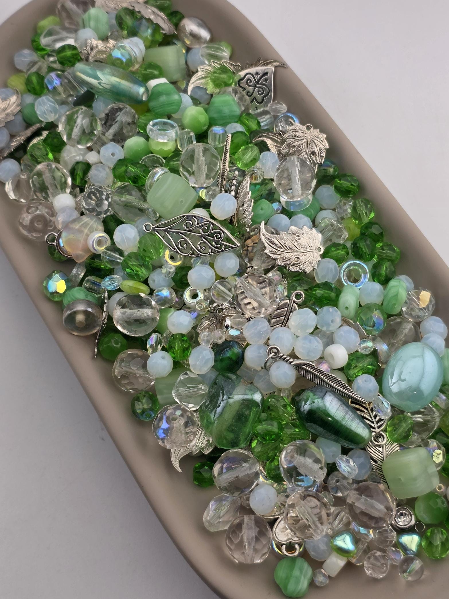 A collection of various colored glass beads, including clear, green, and silver, arranged on a surface.