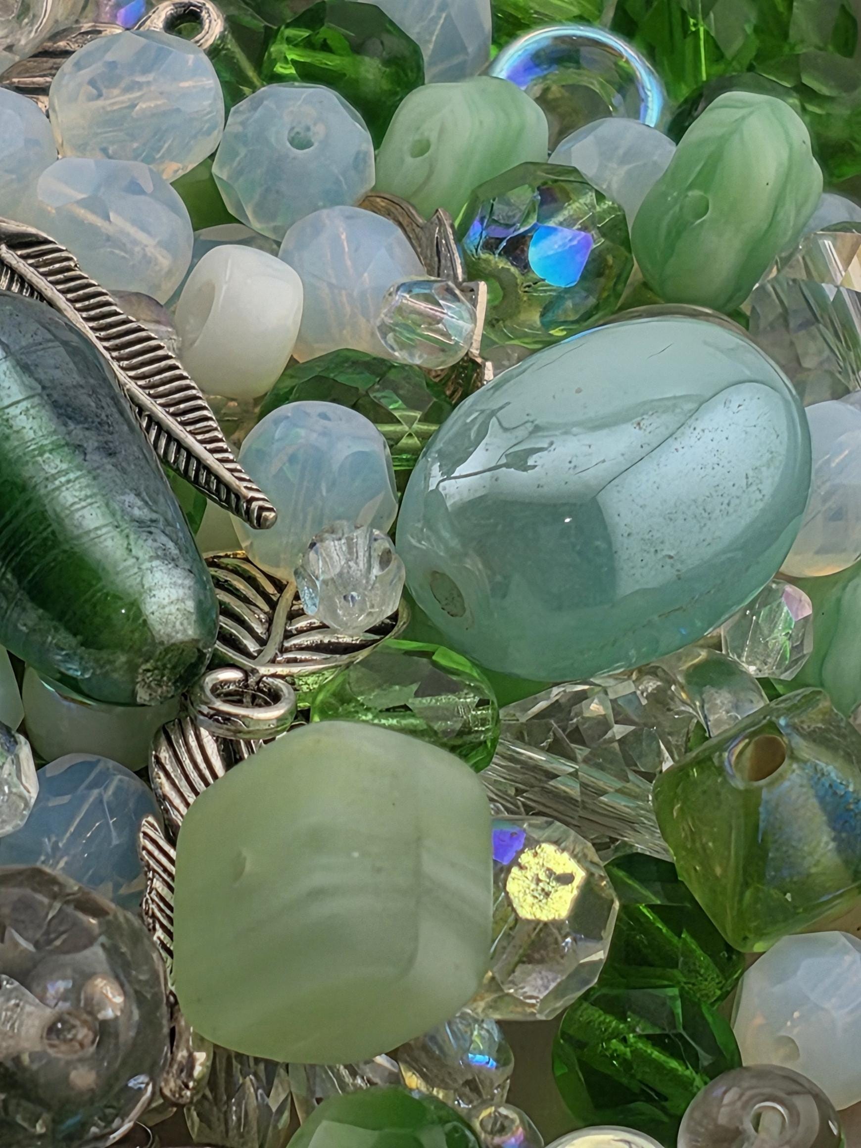 The image is a close-up of various glass beads and stones, including clear, green, and white colors, as well as some with metallic elements.