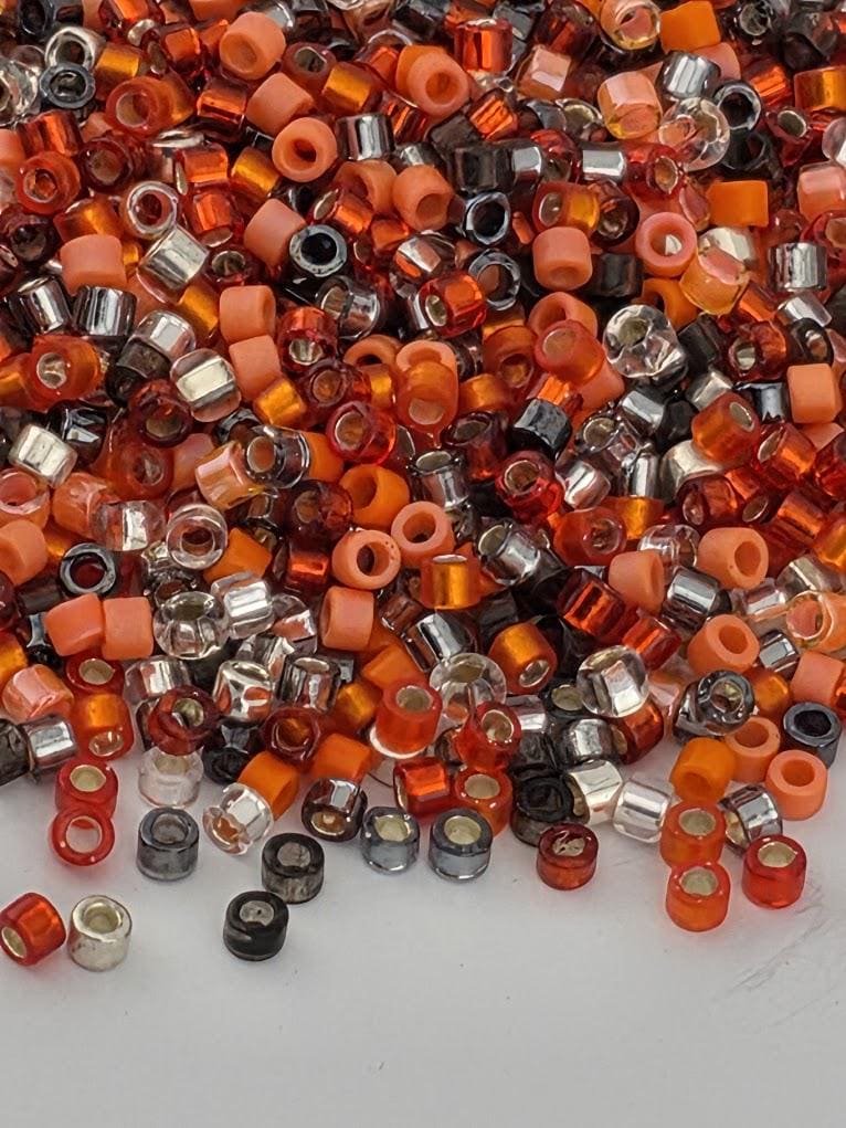 A pile of multicolored beads, including orange, black, and silver, scattered on a dark surface.