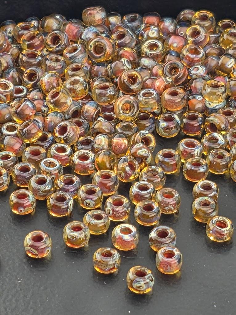 a large pile of small, clear glass beads in various colors, including yellow, orange, and red, scattered on a dark surface.